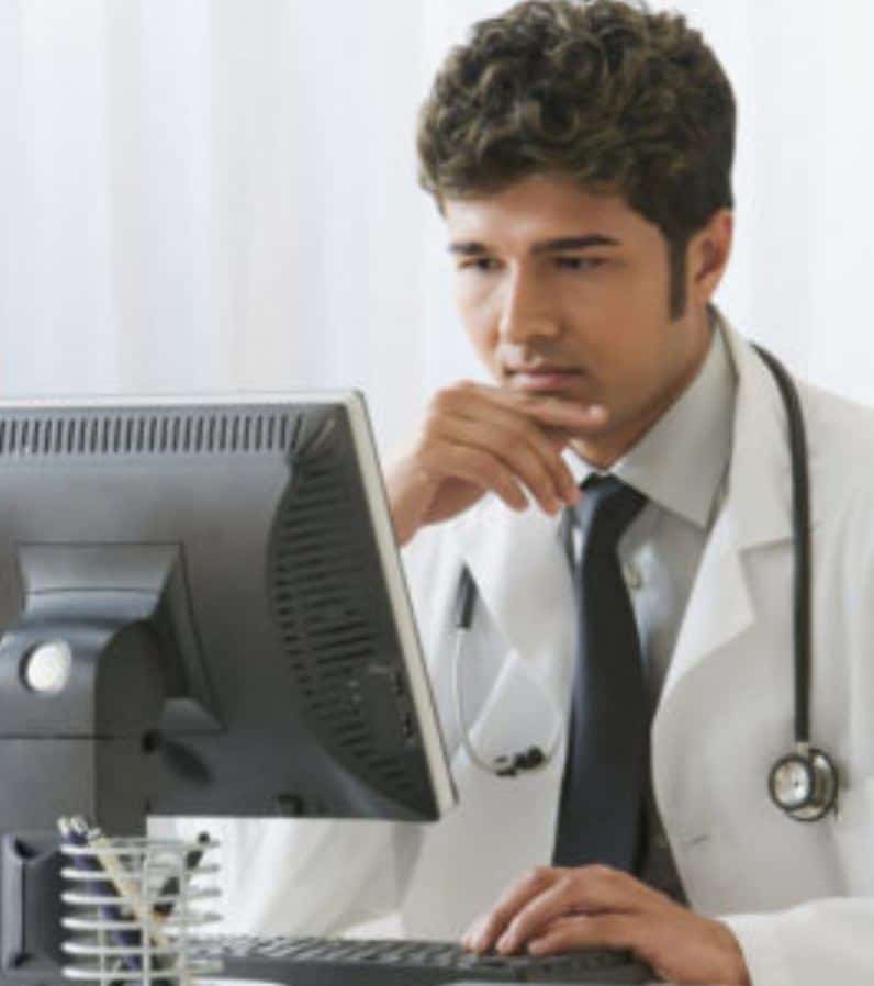 Male doctor with stethoscope around his neck looking at a computer screen