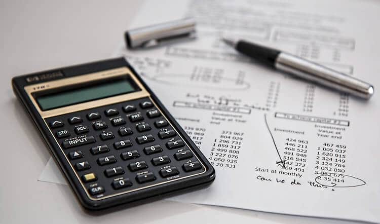 Calculator, open pen and a paper with typed numbers and scribbled notes