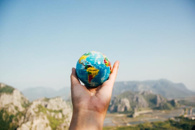 Hand holding a small globe with mountains in the background