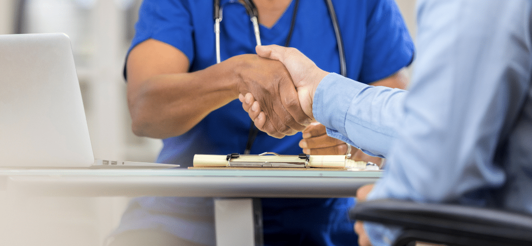 A doctor shakes hands with a patient at a desk