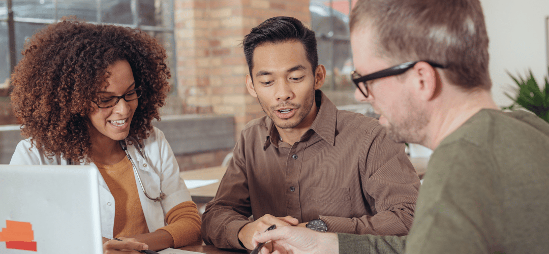 Three people sitting around a table with a laptop